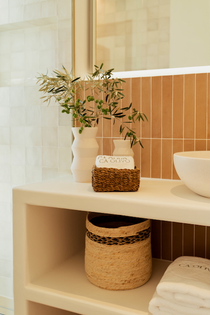 Badkamerdetail met een ingebouwd wastafelmeubel, verticale terracotta tegels en open schappen. Natuurlijke texturen en rieten manden zorgen voor een serene mediterrane sfeer.