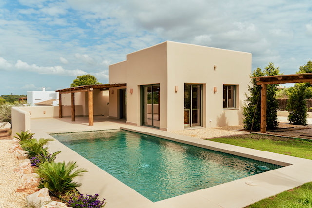 Buitenaanzicht van de moderne villa met rechthoekig zwembad, zandkleurige gevel en een rustieke houten pergola op het ruime terras.