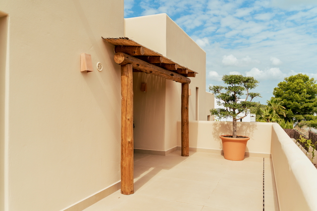 Buitenterras met een rustieke houten pergola, rieten dak en neutrale vloertegels, voorzien van een decoratieve boom in een terracotta pot.