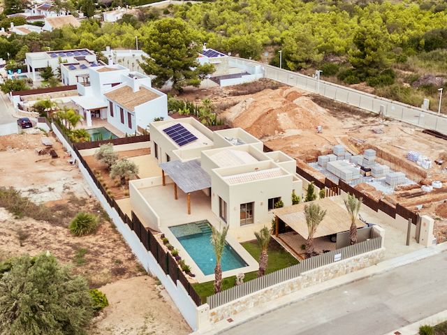 Luchtfoto van de moderne villa met zonnepanelen, een rechthoekig zwembad en een aangelegde tuin met pergola in de groene omgeving van Jávea.