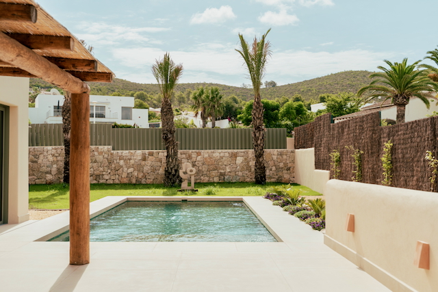 Rechthoekig zwembad op een terras van keramische tegels, omgeven door natuurstenen muren, een mediterrane tuin met palmbomen en een rustieke houten veranda.