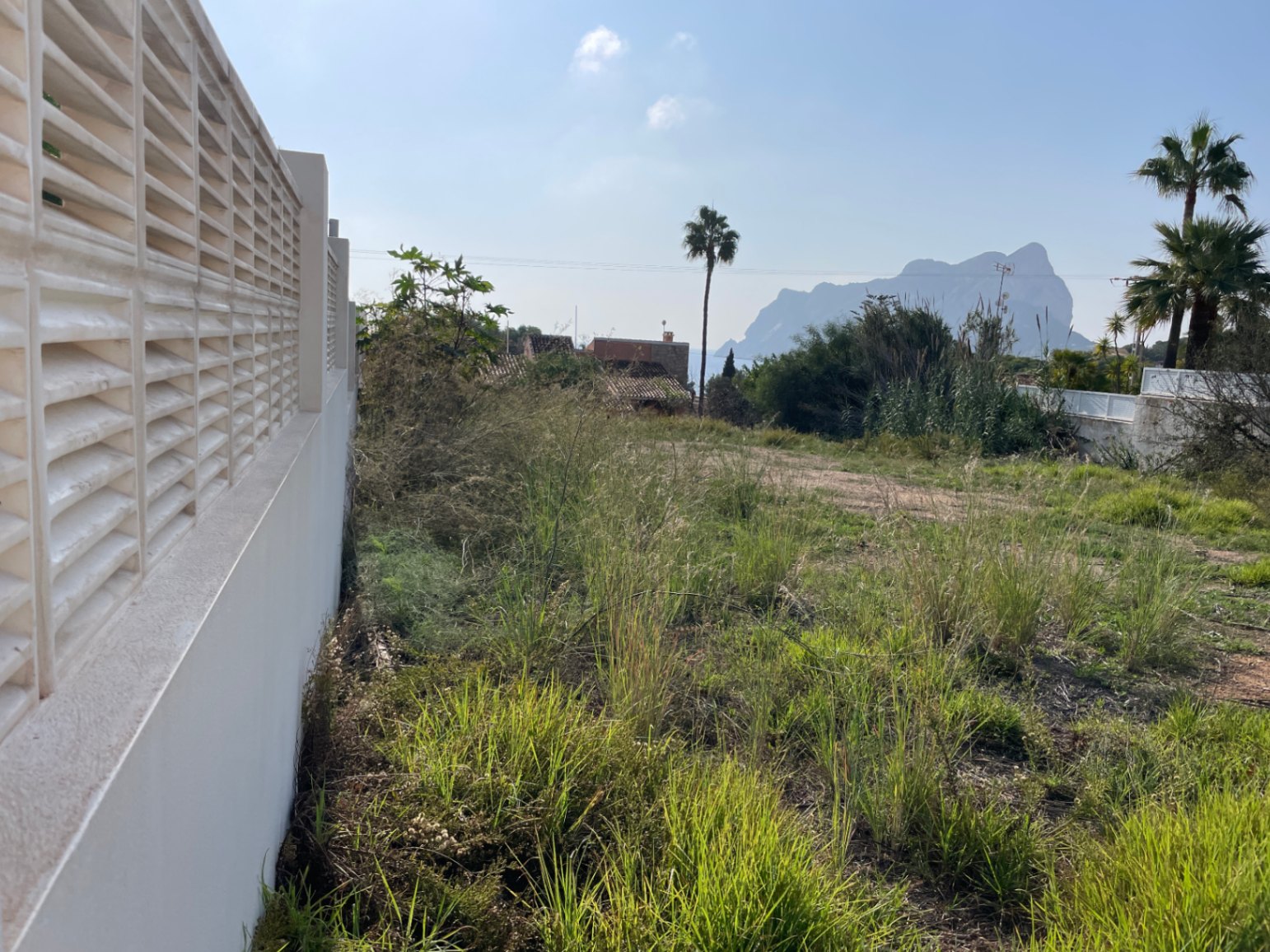 Bouwgrond van 856 m² in Bassetes, Calpe, voorzien van een witte tuinmuur en een onbelemmerd uitzicht op de rots van Peñón de Ifach.