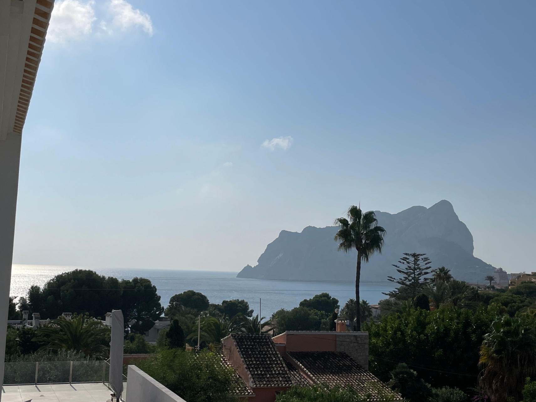 Panoramisch uitzicht op de Middellandse Zee en de Peñón de Ifach vanaf een verhoogd terras met glazen balustrades en weelderige begroeiing.