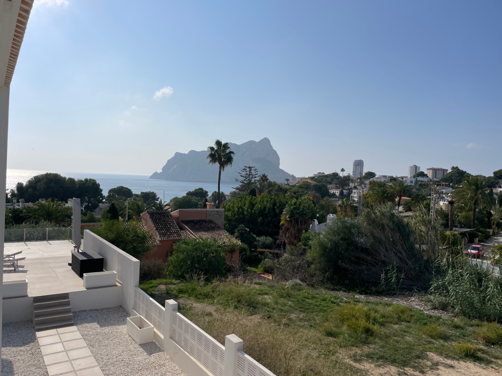 Panoramisch uitzicht op de Peñón de Ifach en de Middellandse Zee vanaf een modern terras met lichte tegels, uitkijkend over de groene omgeving van Calpe.