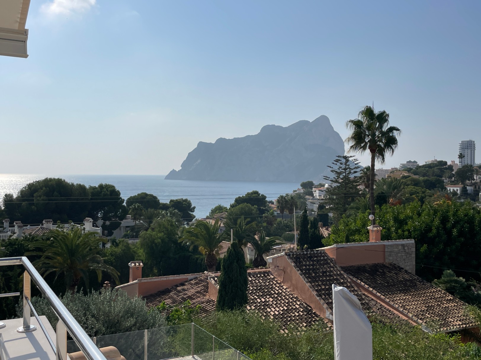 Panoramisch uitzicht op de Peñón de Ifach en de Middellandse Zee vanaf een terras met moderne roestvrijstalen en glazen balustrades.