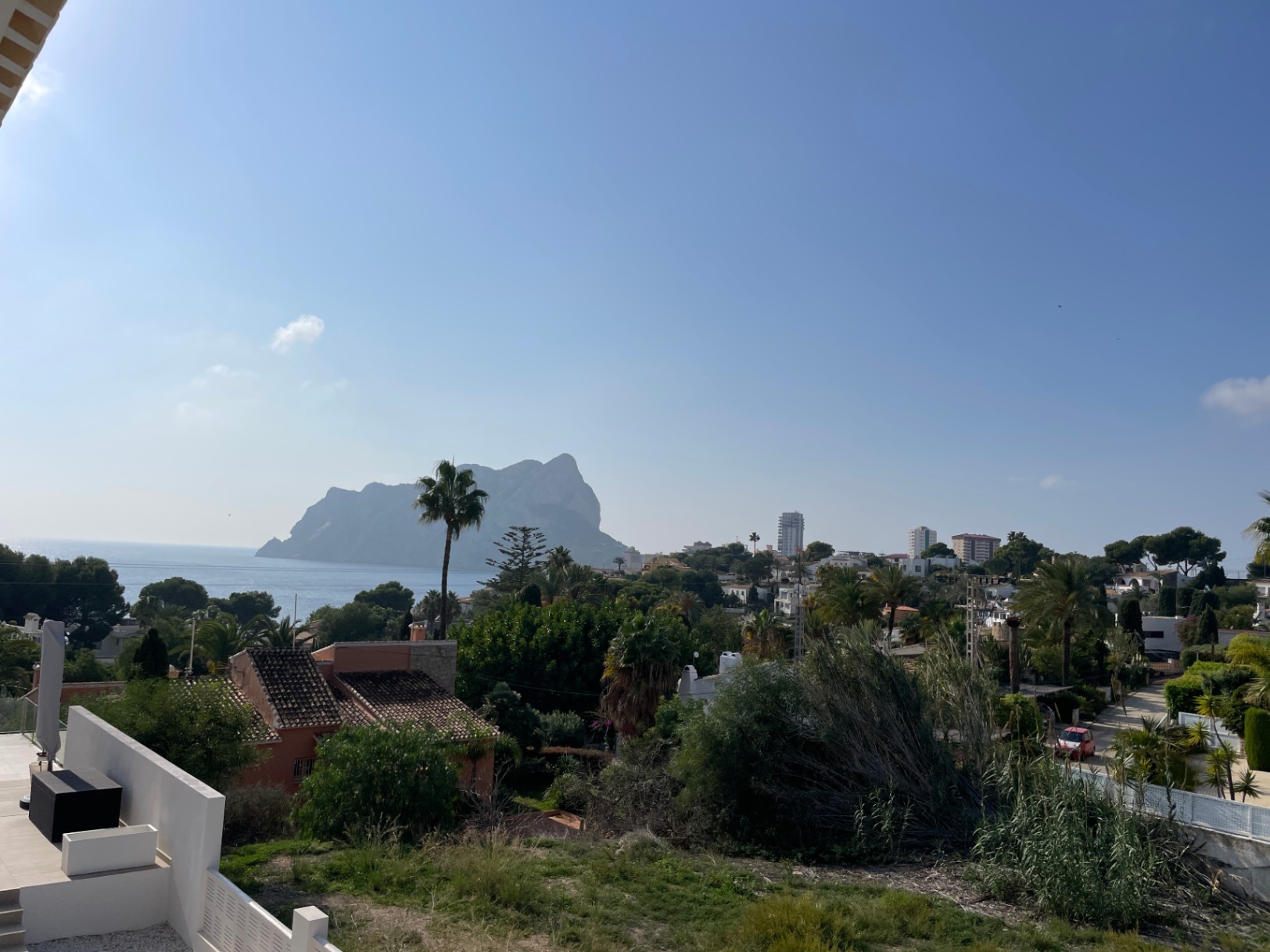 Panoramisch uitzicht op de Peñon de Ifach en de Middellandse Zee vanaf het verhoogde perceel in Bassetes, Calpe, omgeven door weelderig groen en villa's.