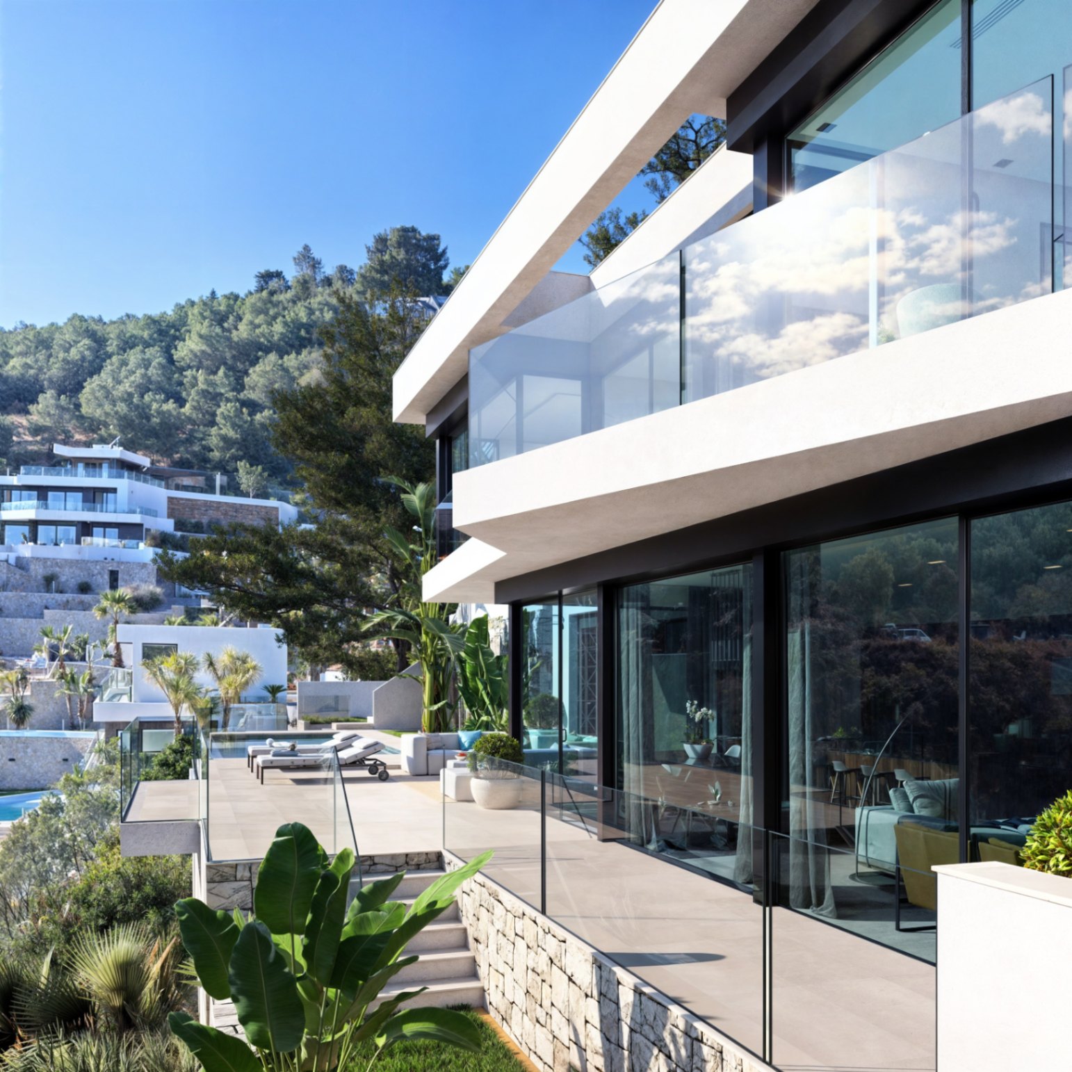 Eigentijdse gevel met grote glaspartijen, glazen balustrades en natuurstenen muren op een verhoogd perceel met mediterrane beplanting.