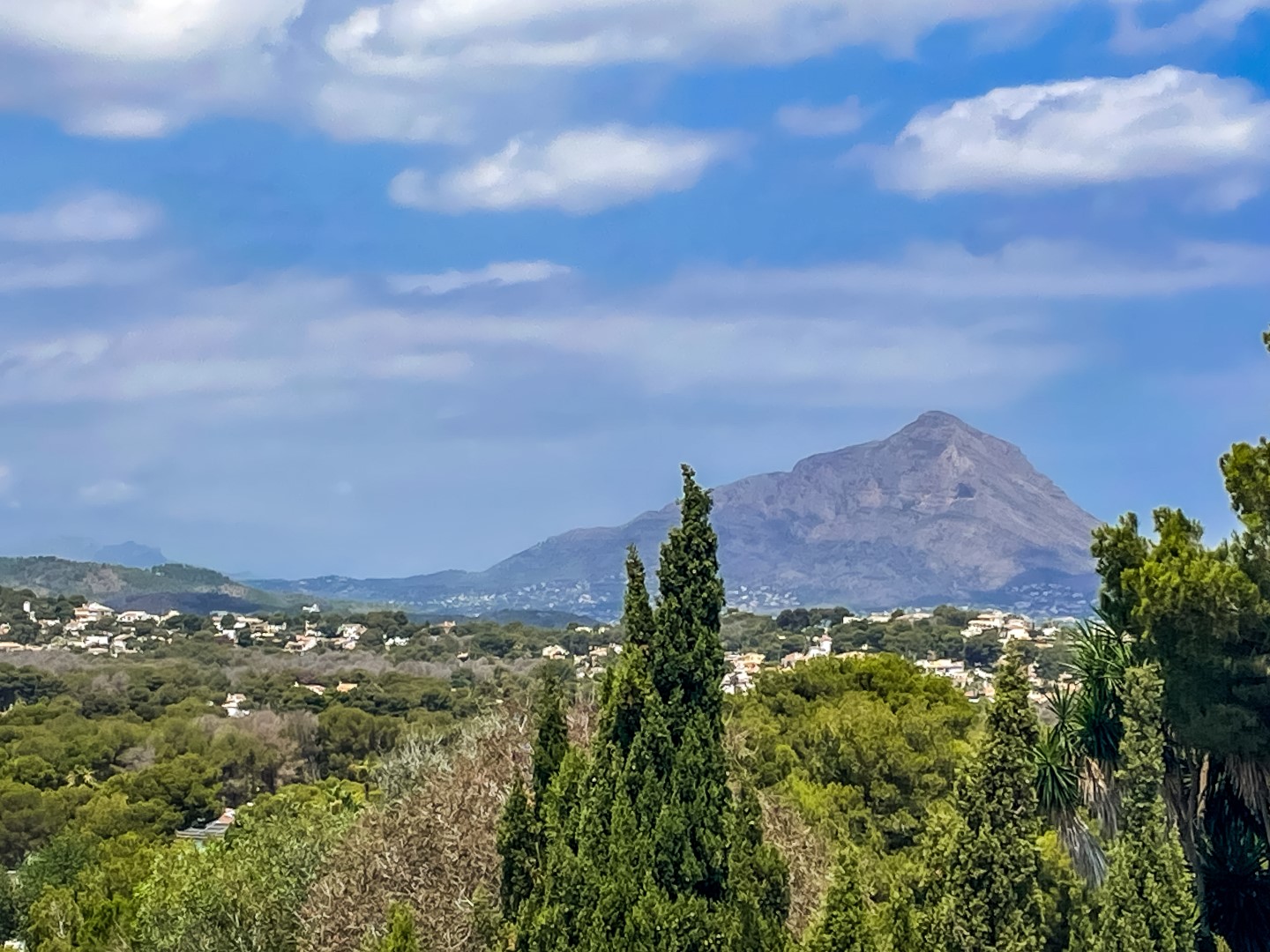 Panoramisch uitzicht vanaf het perceel over de vallei en de Montgó-berg, omgeven door weelderig mediterraan groen en een heldere hemel.