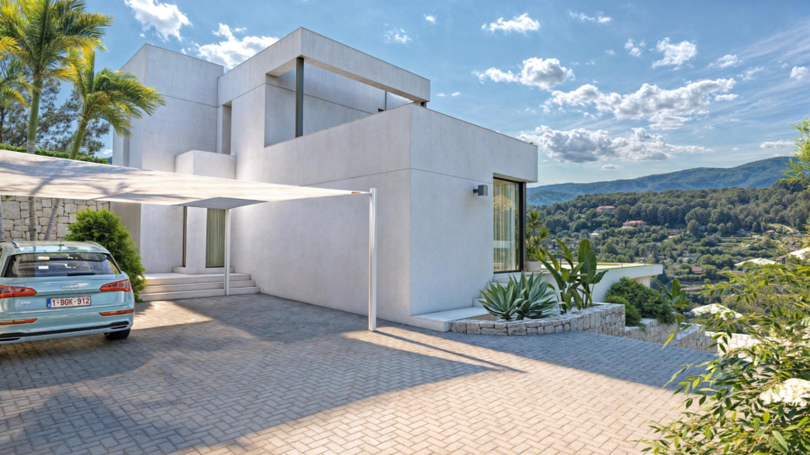 Minimalistische villa met een bestrate oprit, schaduwdoek en natuurstenen muren, met een panoramisch uitzicht op de Sierra de Bernia.