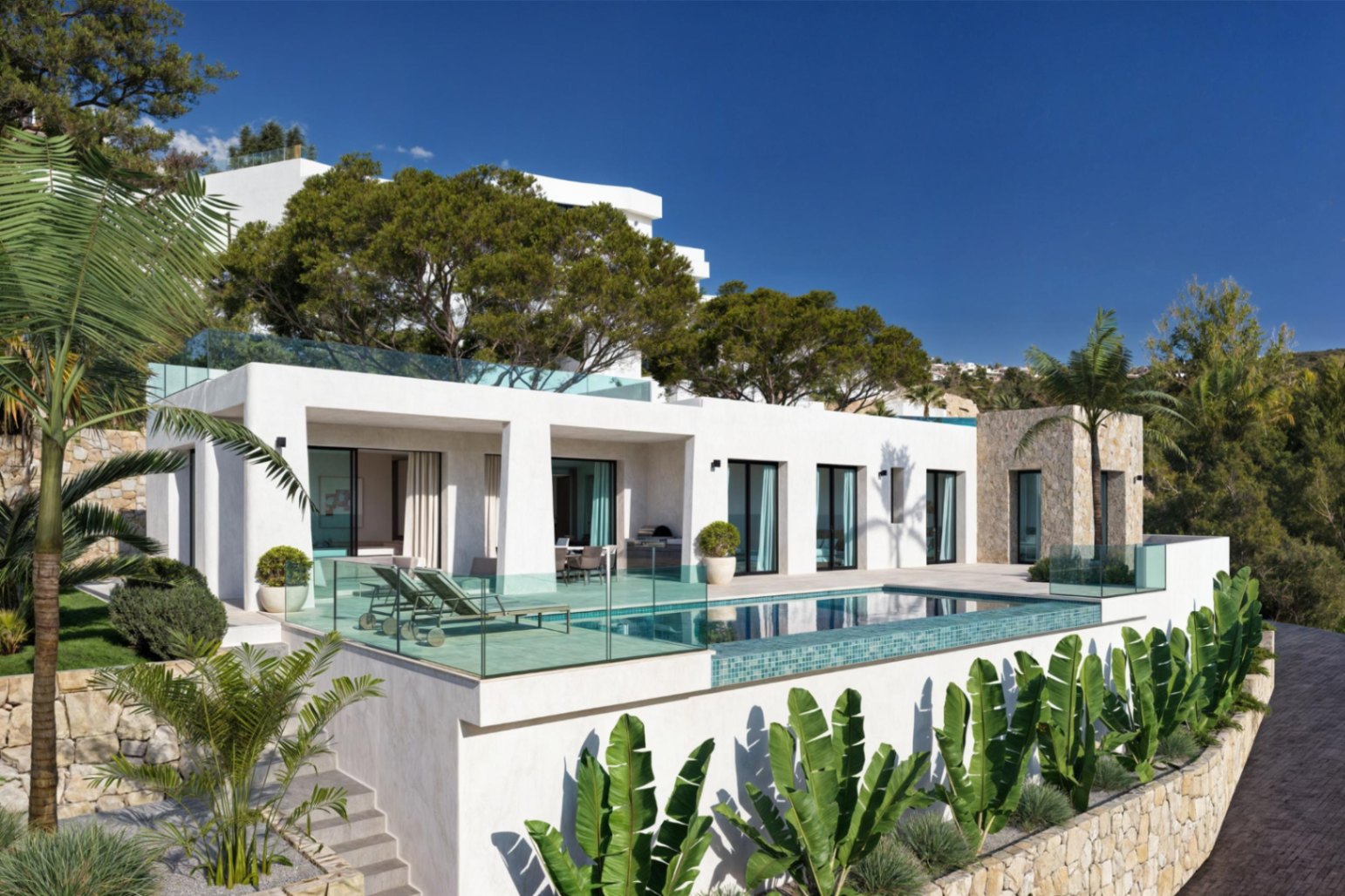 Buitenaanzicht van de villa met zwembad, terras met ligstoelen en een mediterrane tuin met palmbomen.