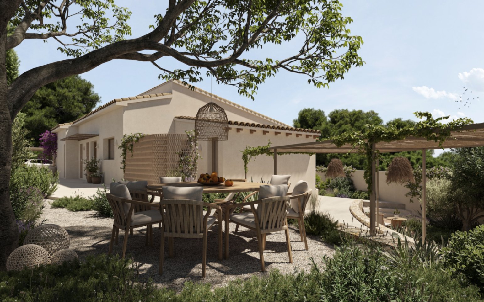 Buiteneethoek in de schaduw van een grote boom, met een ronde houten tafel en gevlochten stoelen op een grindterras naast de mediterrane villa.