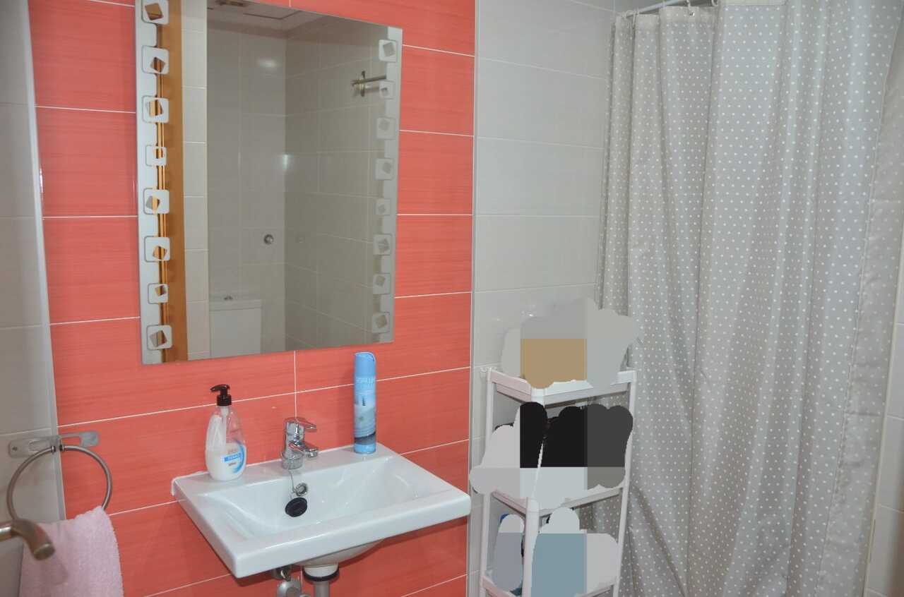 Badkamer met koraalkleurige wandtegels, een witte keramische wastafel en een decoratieve spiegel naast een douchegordijn met stippenpatroon.