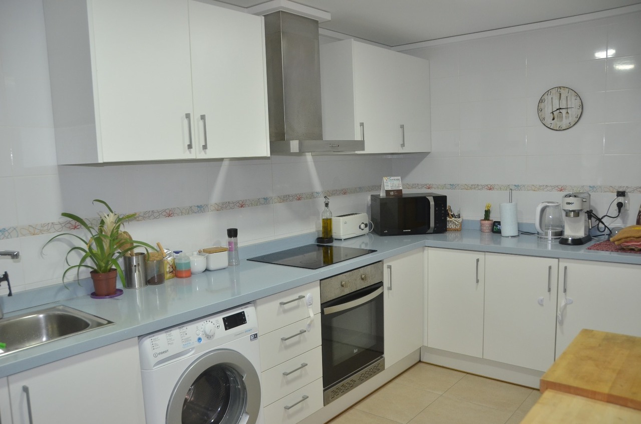 Keuken met witte kasten, een lichtblauw werkblad en inbouwapparatuur waaronder een wasmachine, oven en keramische kookplaat.