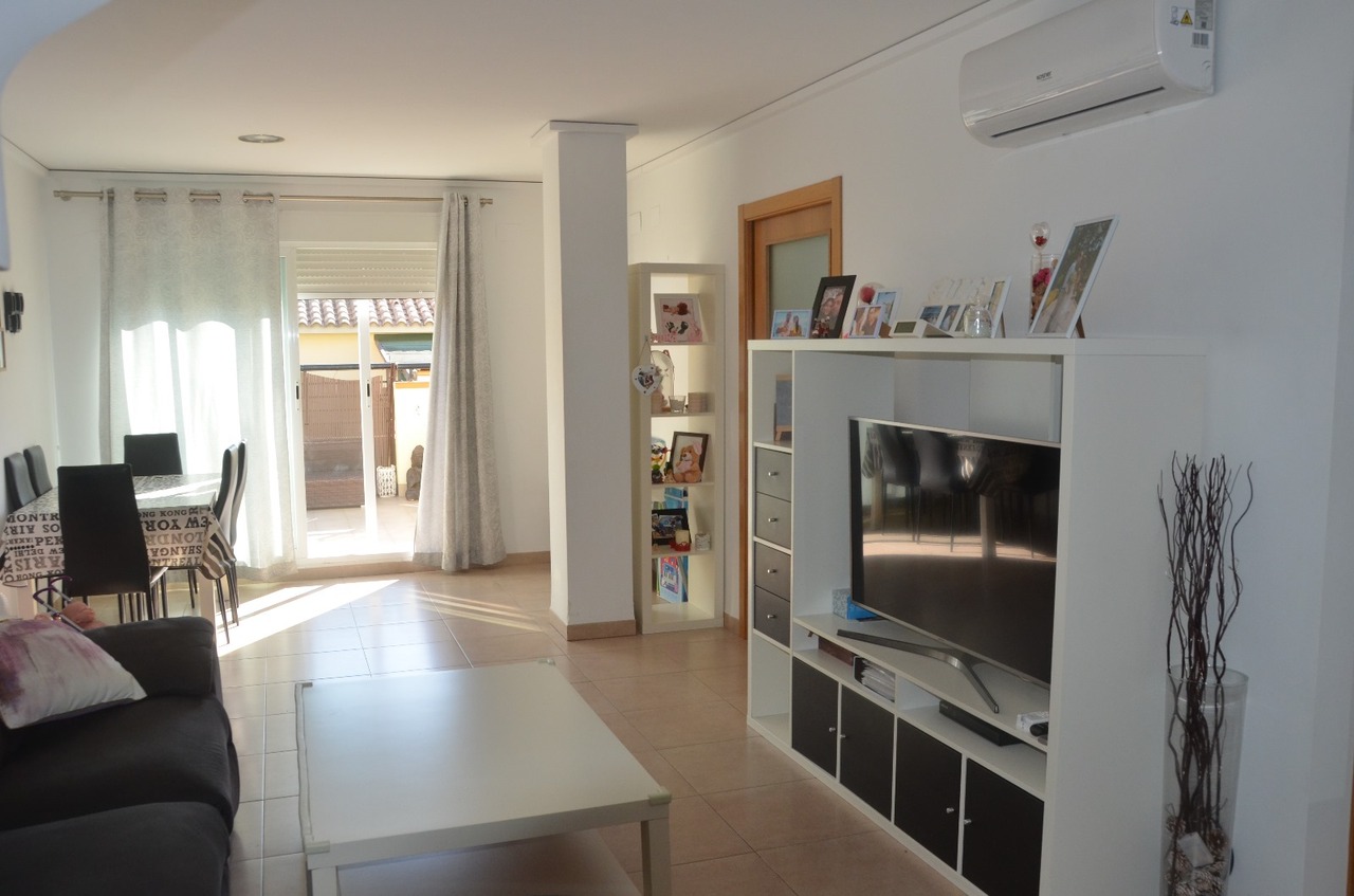 Lichte woon- en eetkamer met tegelvloer, modulair tv-meubel, wandgemonteerde airconditioning en directe toegang tot het buitenterras.
