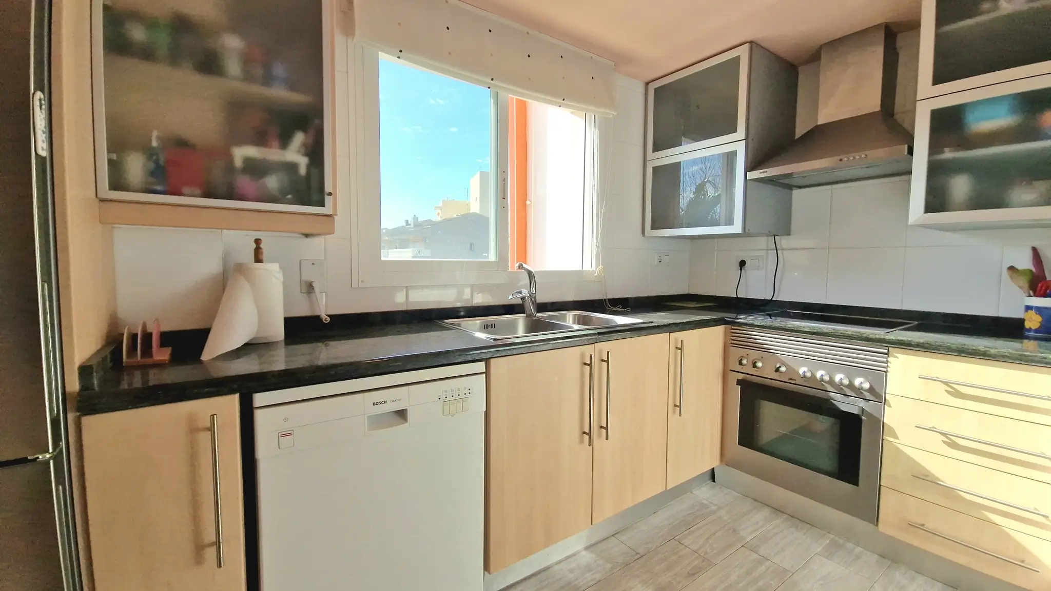 Functionele keuken met lichte houten kasten, een donker granieten werkblad en inbouwapparatuur waaronder een Bosch vaatwasser en een roestvrijstalen oven.