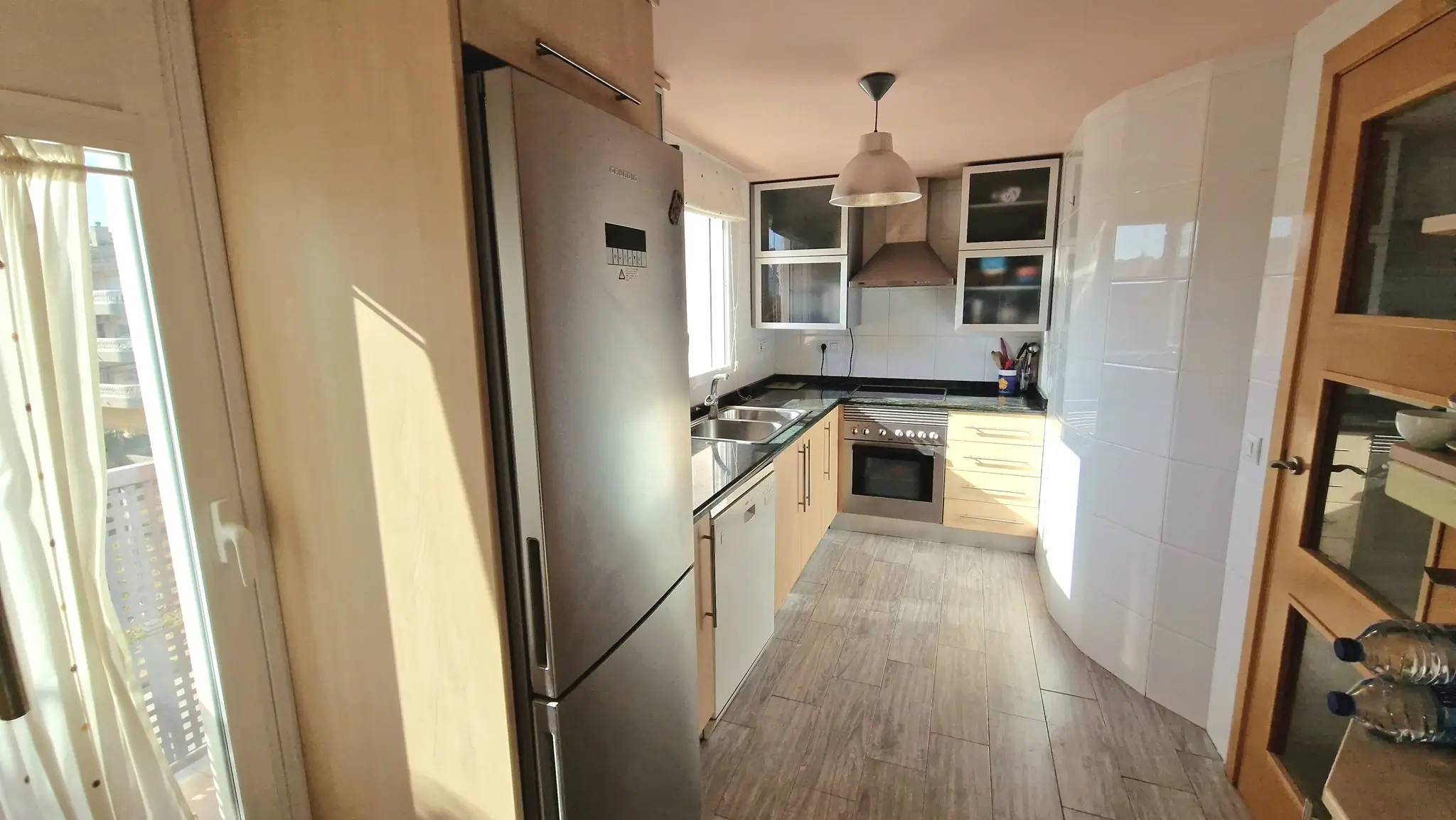 Keuken met licht houten kasten, zwart granieten werkbladen en roestvrijstalen apparatuur. Voorzien van een keramische tegelvloer met houtlook.