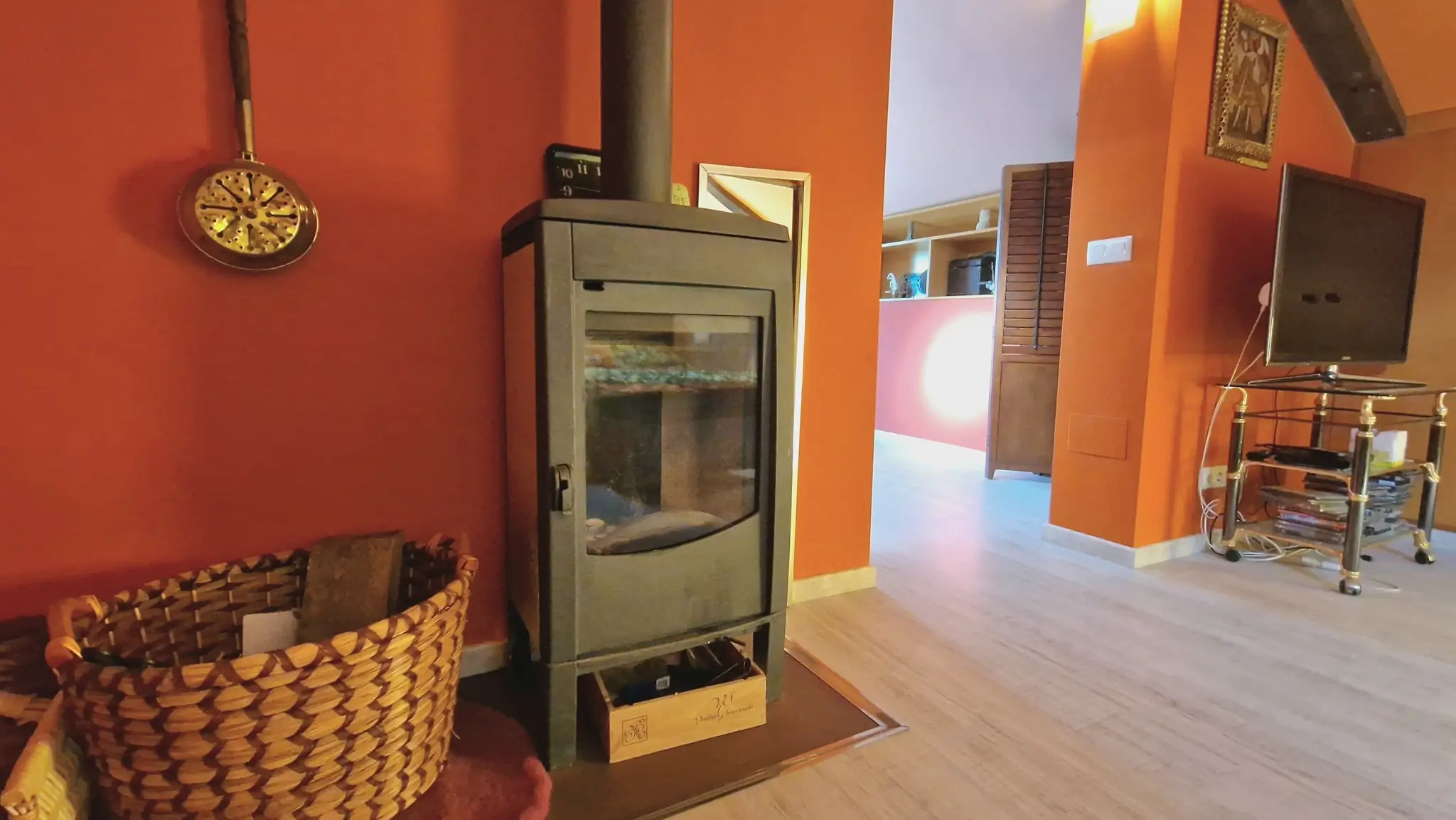 Moderne zwarte houtkachel geplaatst tegen terracotta wanden, met een lichte houten vloer en een traditionele rieten mand voor brandhout.