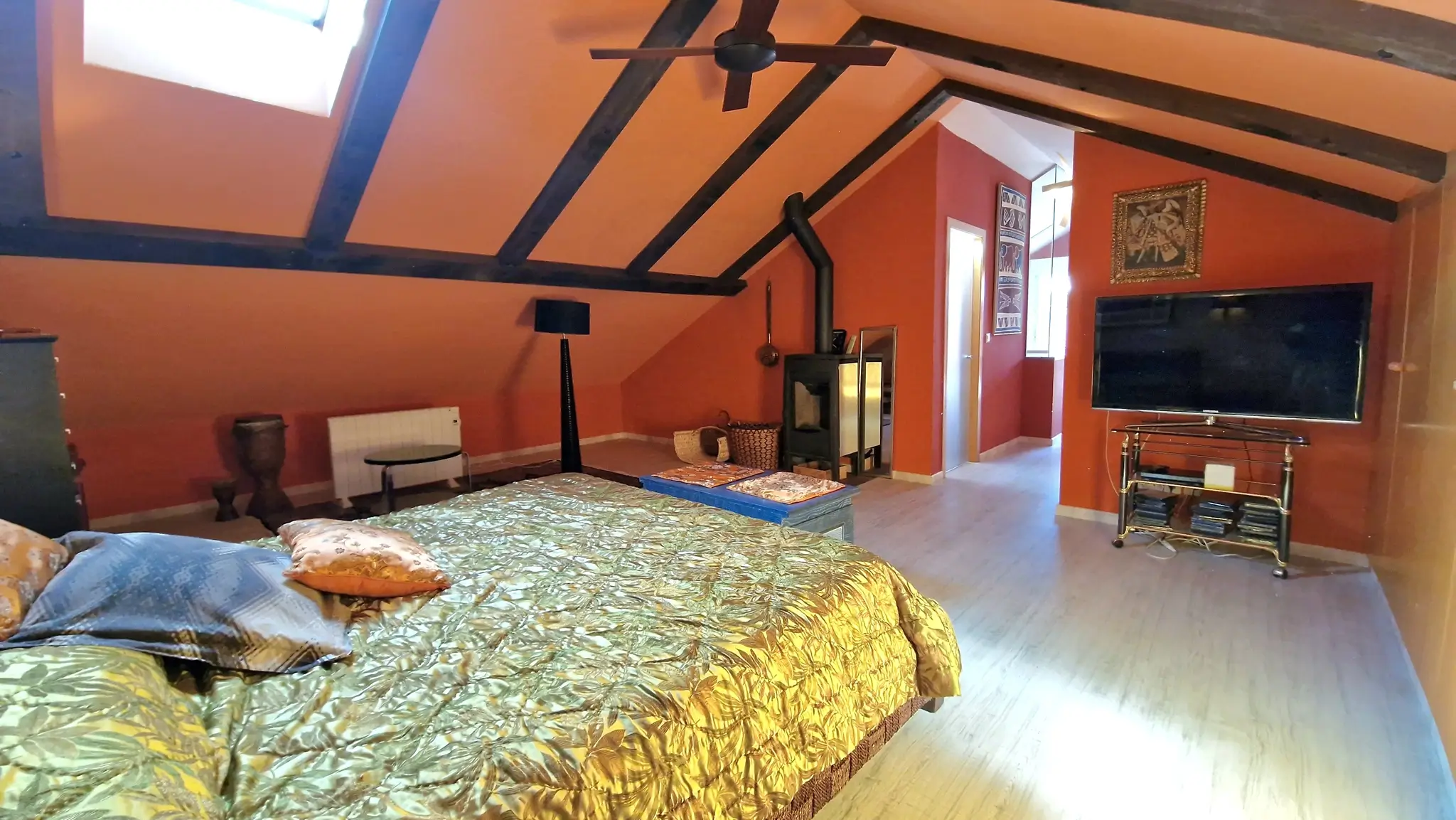 Slaapkamer onder het schuine dak met houten balken, terracotta muren, een houtkachel en een dakraam voor natuurlijke lichtinval.