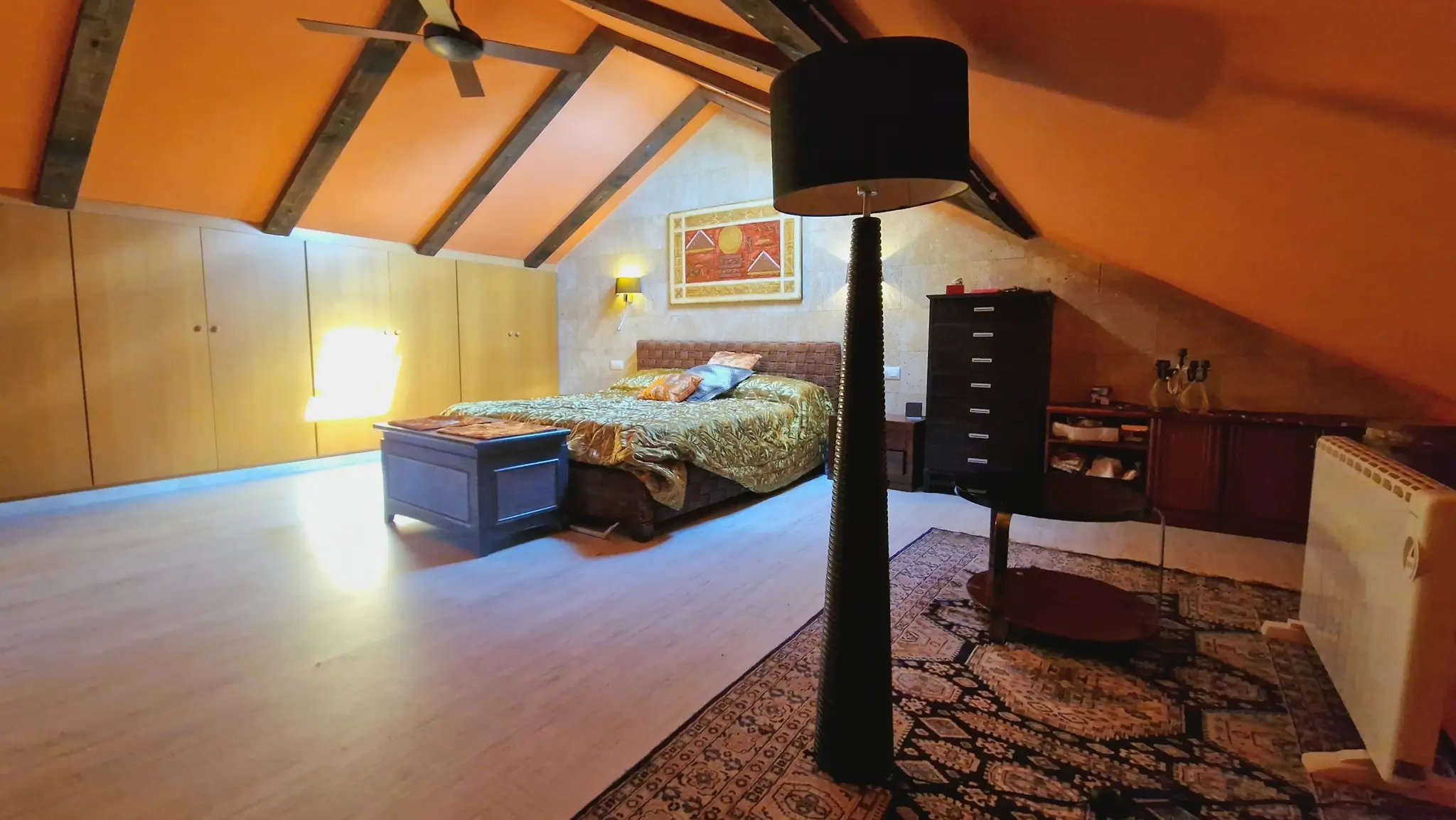Zolderkamer met donkere houten balken, ingebouwde lichthouten kasten en een natuurstenen accentmuur onder het schuine plafond.