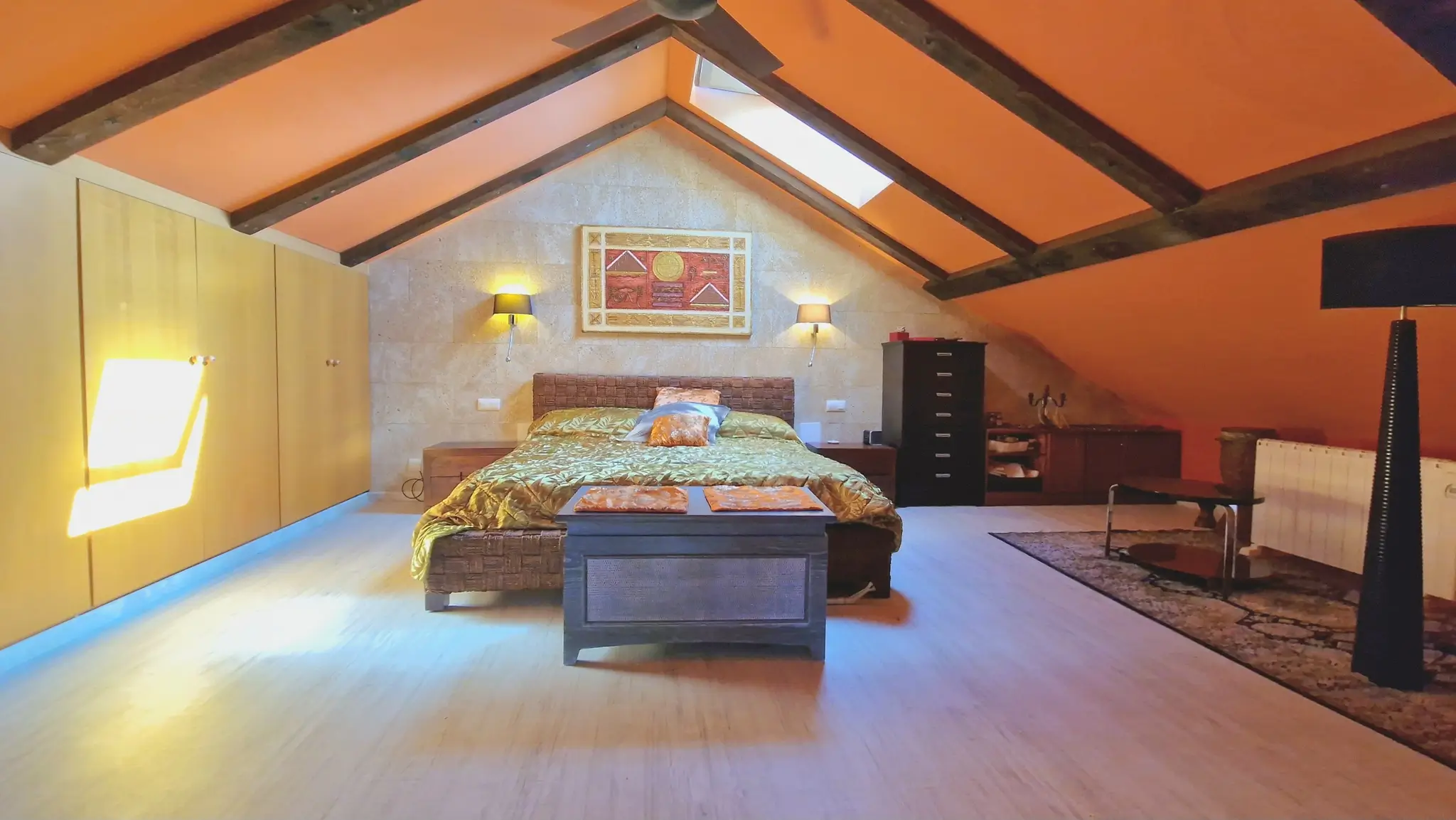 Zolderkamer met donkere houten balken, oranje schuine plafonds, een natuurstenen accentmuur en ruime ingebouwde houten kastenwand.