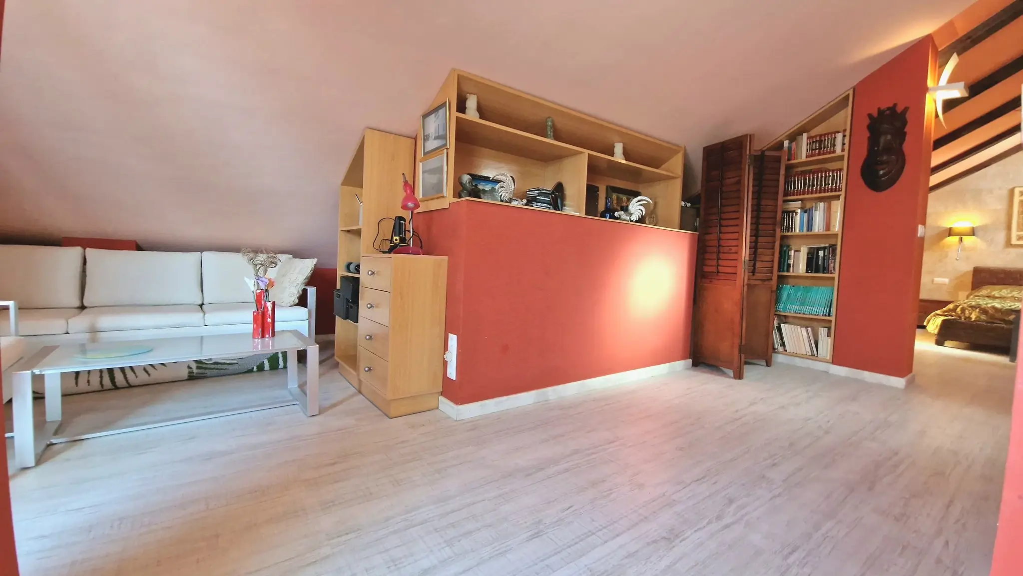 Zolderruimte met terracotta accentmuren, ingebouwde houten kasten en een lichte laminaatvloer onder een schuin dak.