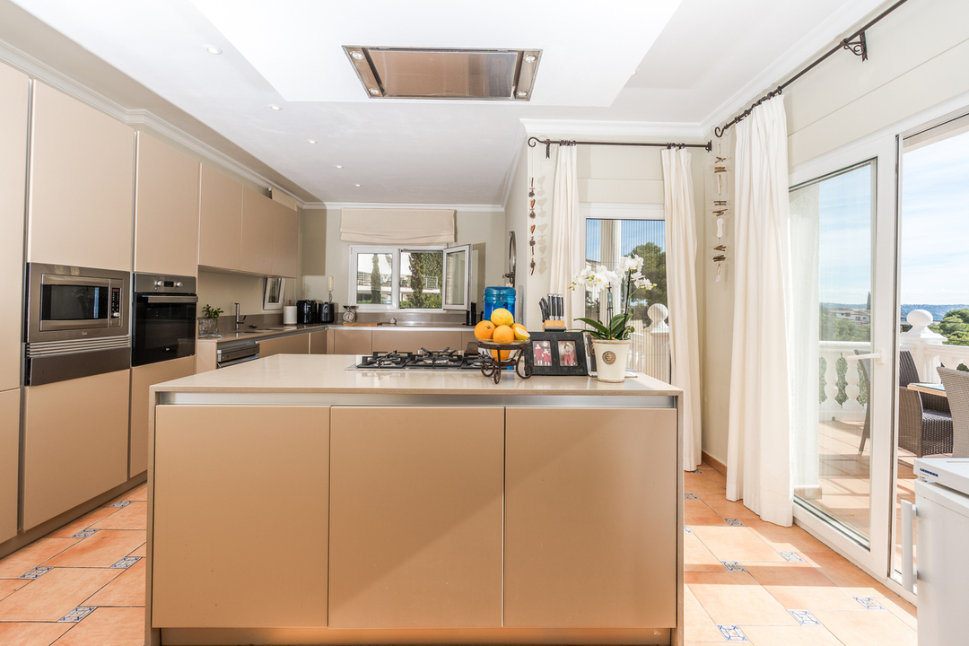 Eigentijdse keuken met kookeiland, inbouwapparatuur en terracotta tegels. De grote schuifpui zorgt voor veel lichtinval en directe toegang tot het terras.