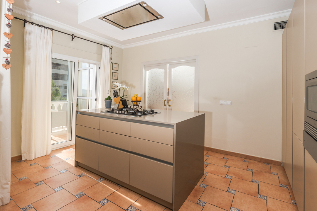 Keuken met kookeiland, gaskookplaat, terracotta tegelvloer met decoratieve details en toegang tot het buitenterras.