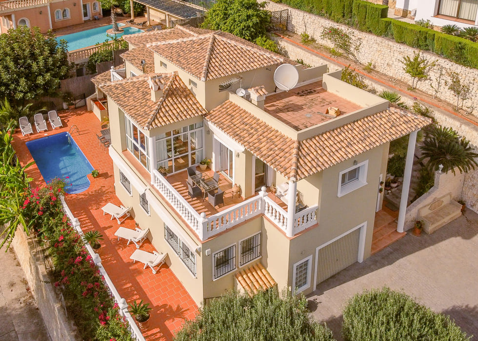 Luchtfoto van een mediterrane villa met terracotta daken, privézwembad en diverse terrassen met witte balustrades en een eethoek in de buitenlucht.