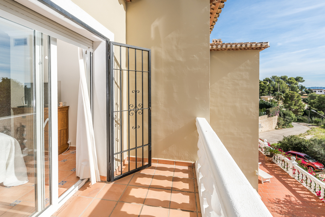 Privébalkon met terracotta vloertegels en witte balustrade, voorzien van een smeedijzeren beveiligingshek en uitzicht op het mediterrane landschap.