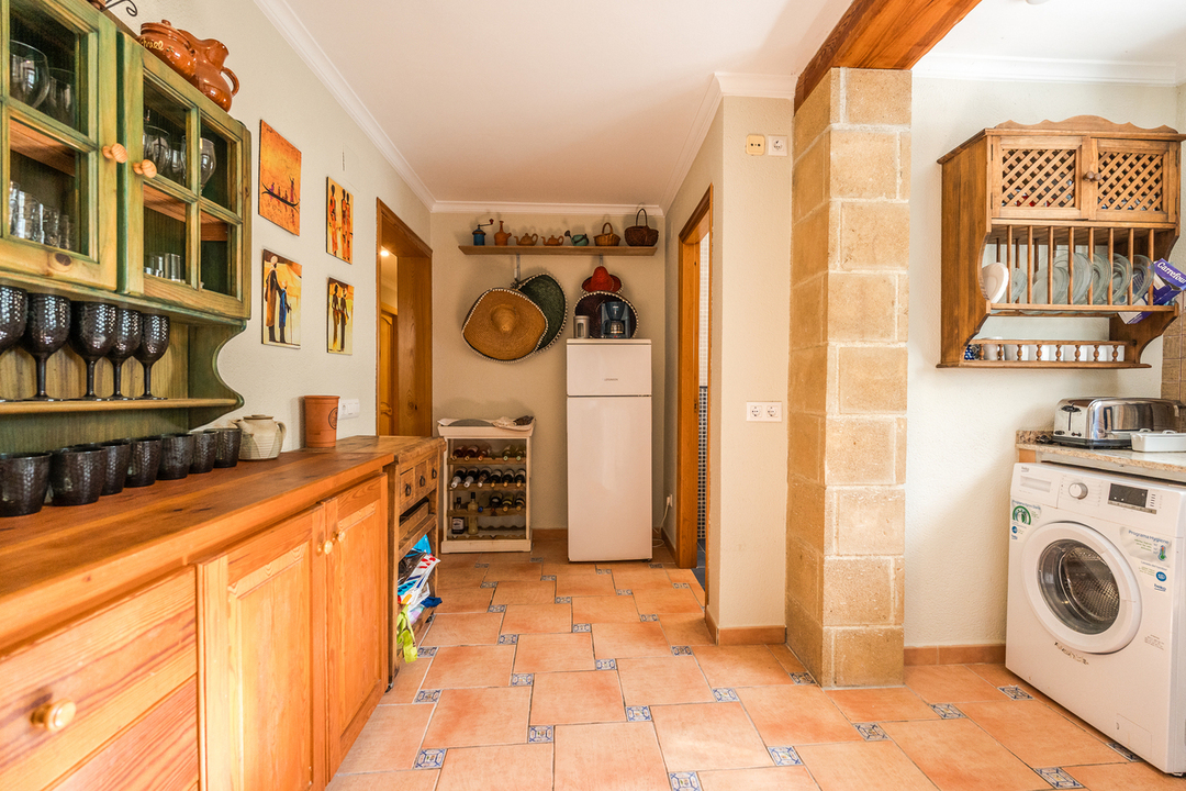 Rustieke keuken met houten kasten, terracotta tegelvloer met blauwe details, een natuurstenen pilaar en een geïntegreerde wasruimte.