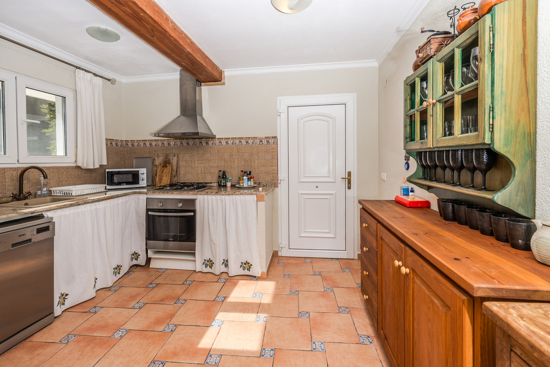 Rustieke keuken met terracotta vloertegels, houten plafondbalken, granieten werkbladen en een houten dressoir met een groene vitrinekast.