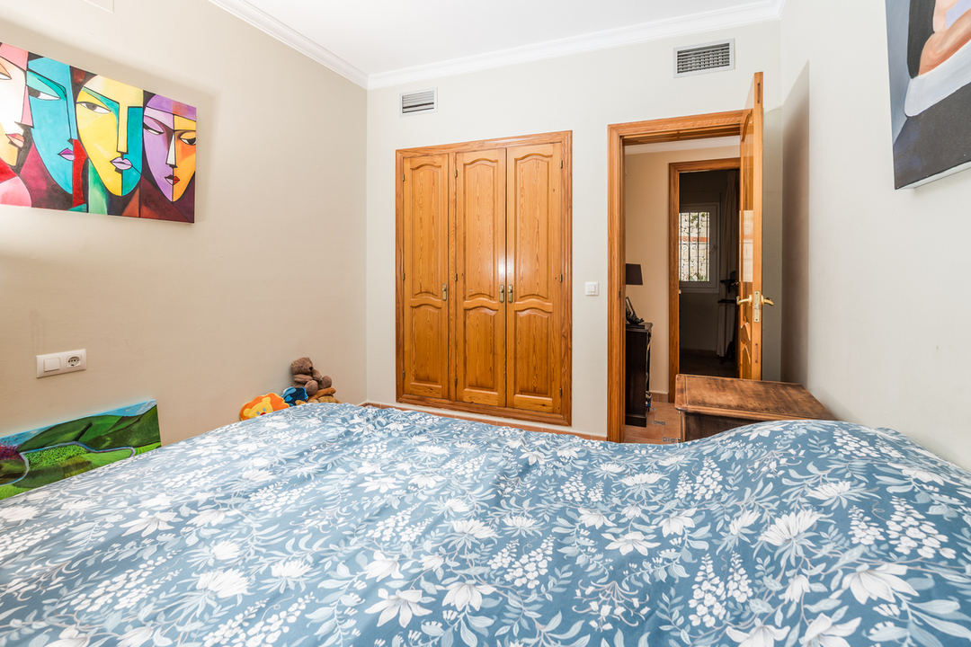 Slaapkamer met een houten inbouwkast, lichte wanden met moderne kunst en een bed met blauw-wit gebloemd beddengoed.