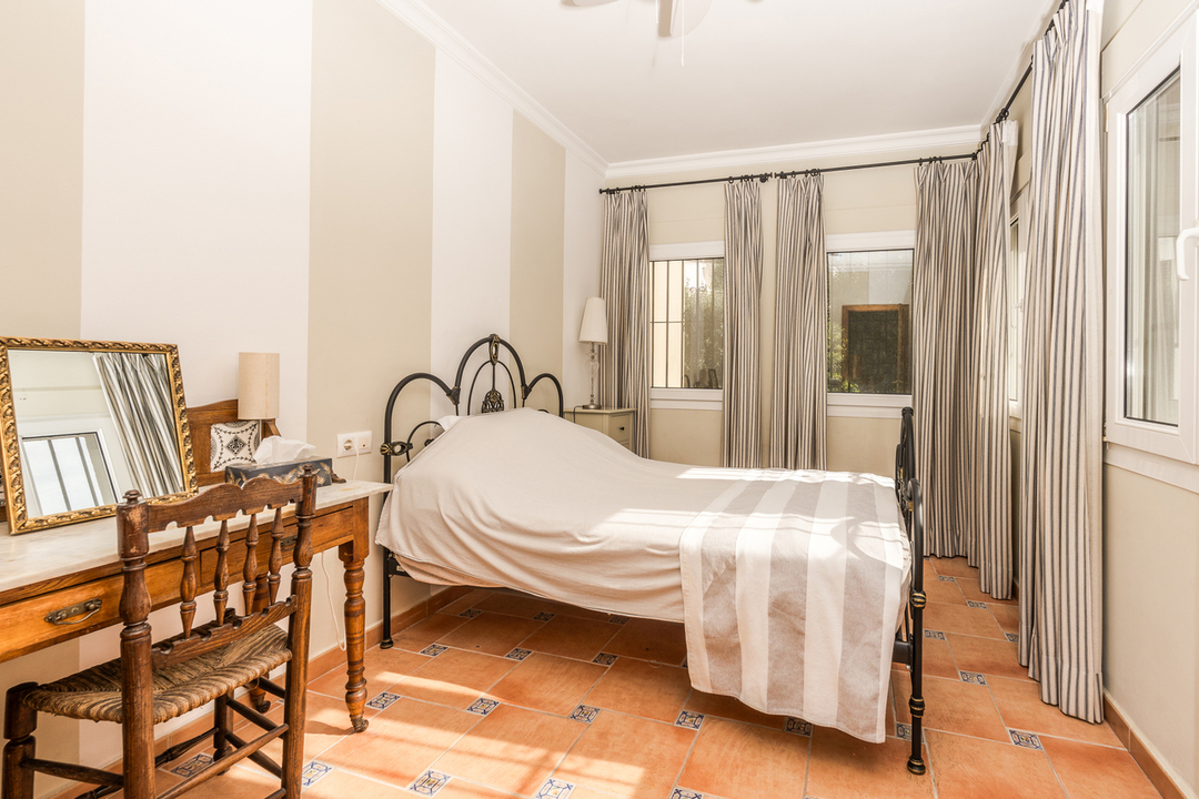 Slaapkamer met een zwart smeedijzeren bed, gestreept behang en een terracotta vloer met decoratieve tegels. Inclusief een klassiek houten bureau met spiegel.