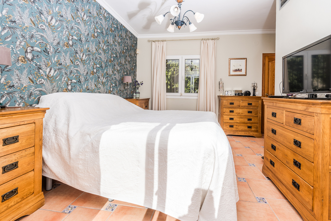 Slaapkamer met tropisch behang, bijpassende houten ladekasten en een terracotta vloer met decoratieve blauwe tegelaccenten.