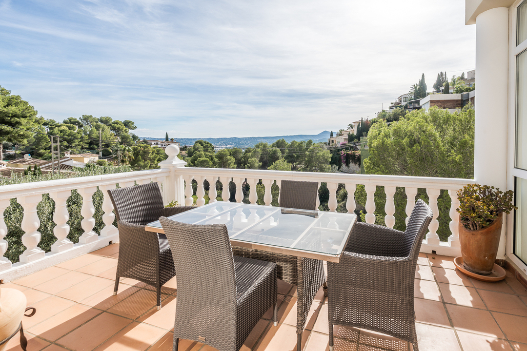 Terras met terracotta tegels en witte balustrade, voorzien van een rieten eethoek met weids uitzicht over de vallei en de bergen.