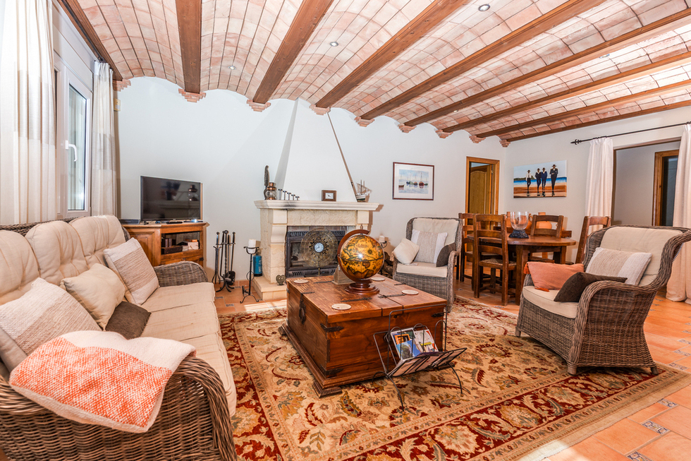 Woonkamer met een Catalaans gewelfd plafond, houten balken, een stenen open haard en rieten meubels op een terracotta tegelvloer.