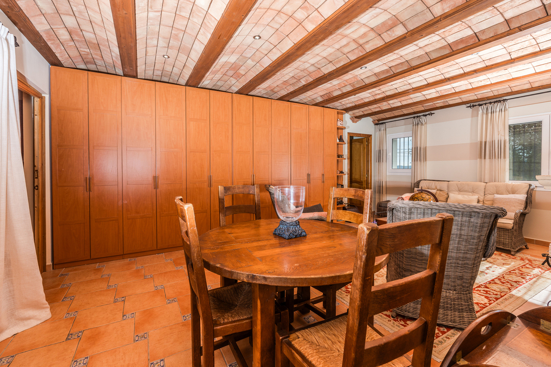 Woonkamer met een traditioneel Catalaans gewelfd plafond, houten balken, terracotta vloertegels en een grote op maat gemaakte houten kastenwand.