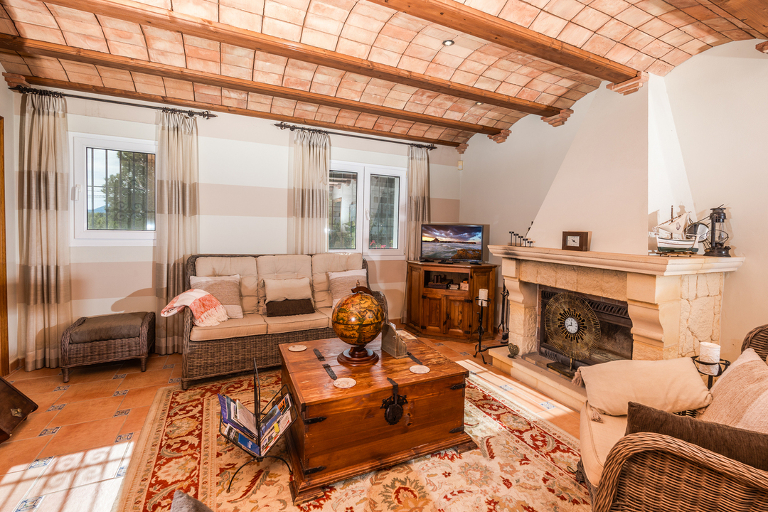 Woonkamer met een traditioneel Catalaans gewelfd plafond met houten balken, een stenen schouw en terracotta vloertegels met decoratieve accenten.
