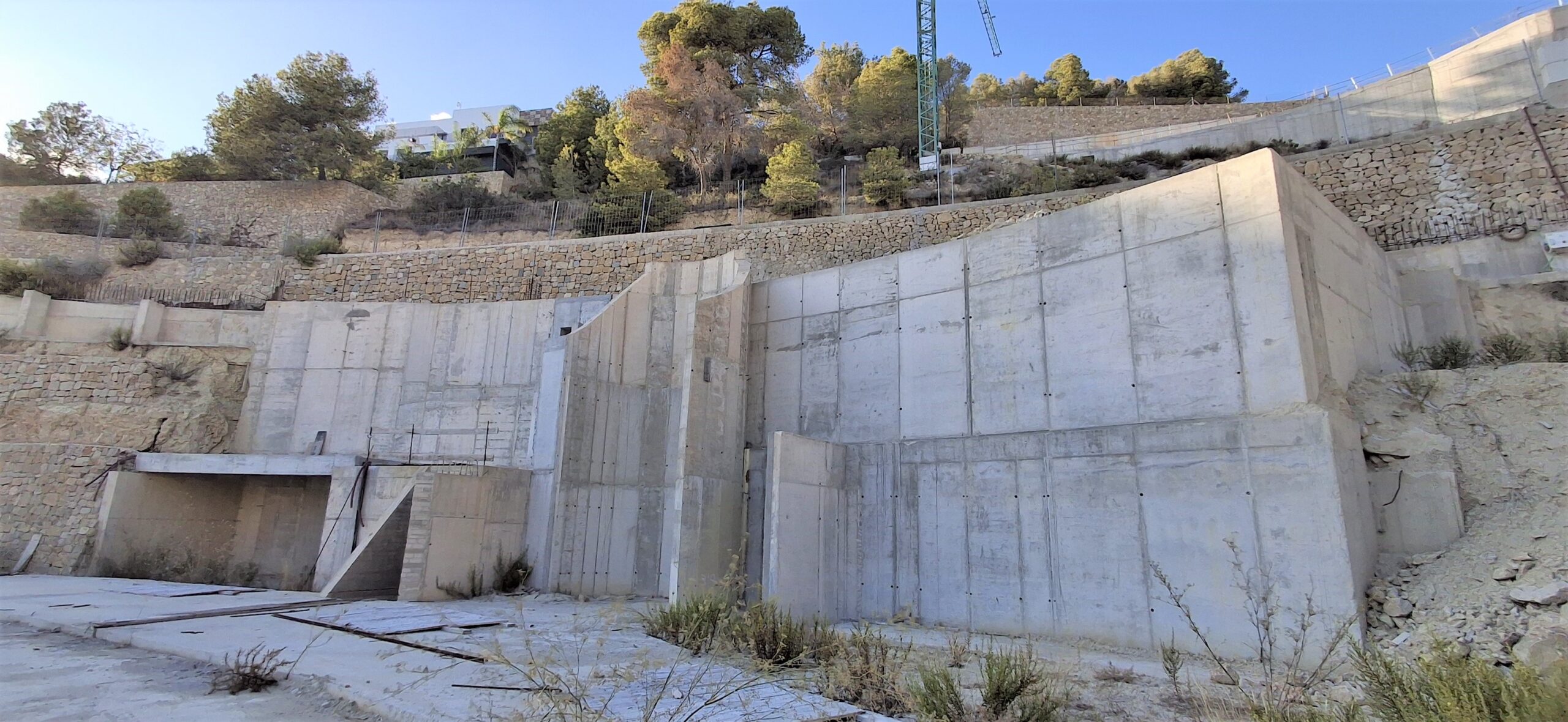 Zicht op de steunmuren van gewapend beton en stenen terrassen geïntegreerd in een hellend perceel met mediterrane vegetatie.