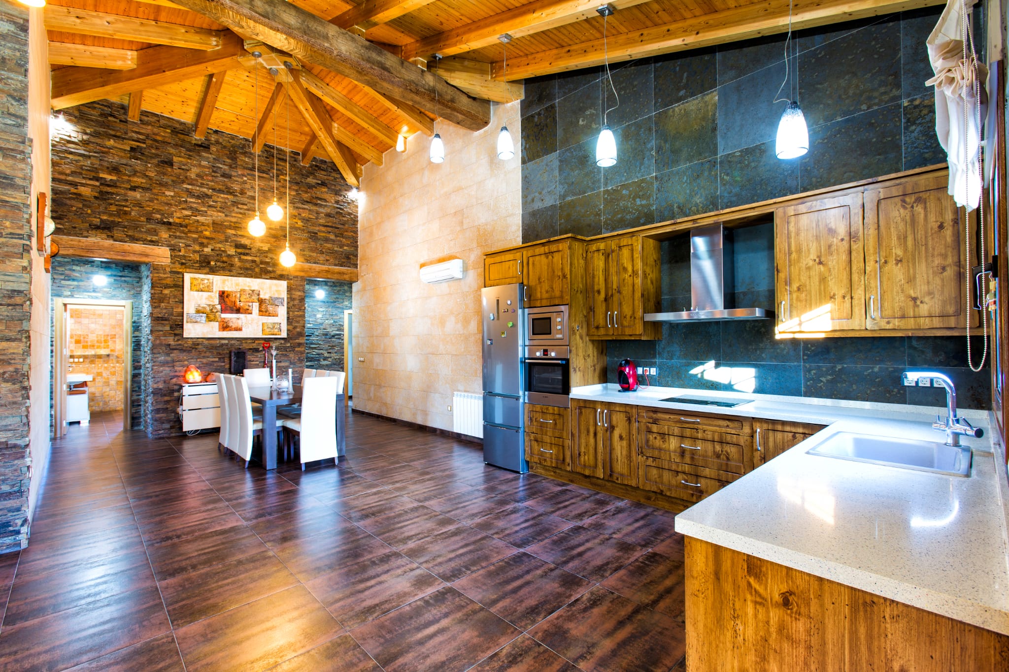 Open keuken en eetkamer met hoog houten plafond, natuurstenen wanden, rustieke houten kasten en roestvrijstalen inbouwapparatuur.