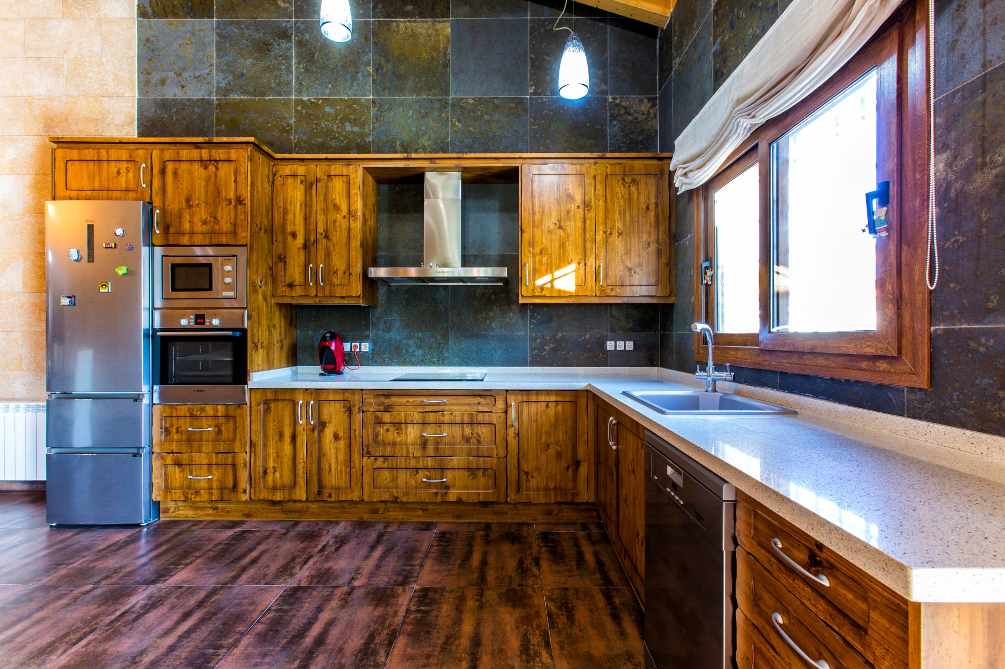 Rustieke keuken met houten kasten, donkere natuurstenen wandtegels en een licht werkblad, voorzien van rvs-inbouwapparatuur en natuurlijke lichtinval.
