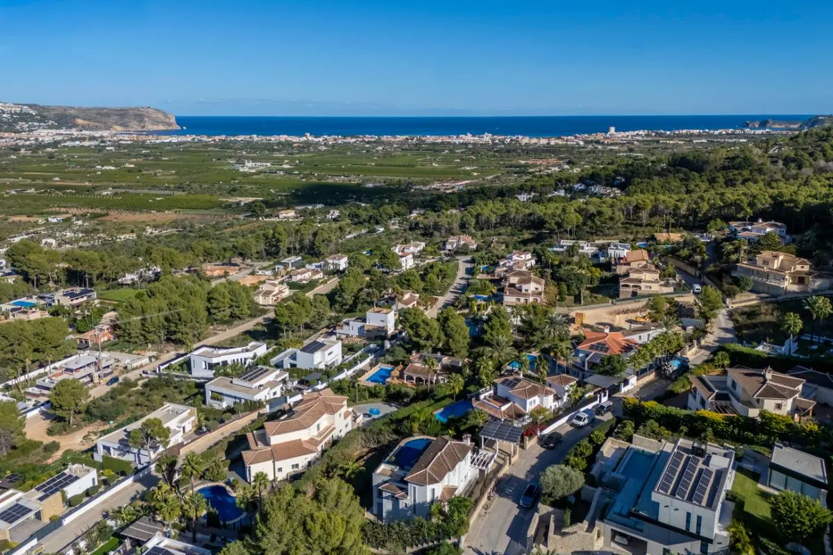 Luchtfoto van een residentiële wijk op een heuvel met villa's, privézwembaden en zonnepanelen, met panoramisch uitzicht over de vallei en de zee.