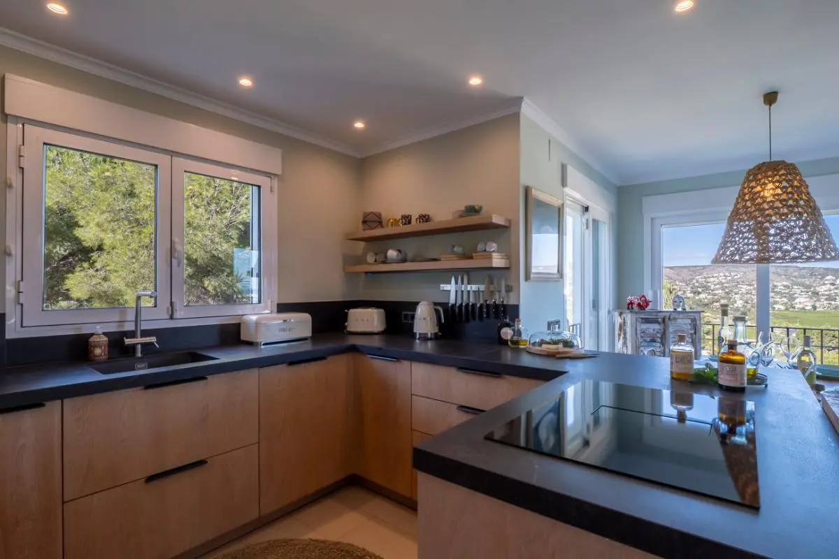 Moderne keuken met lichte houten kasten, donkere werkbladen en een inductiekookplaat. Grote ramen bieden natuurlijk licht en uitzicht op de pijnbomen en de vallei.