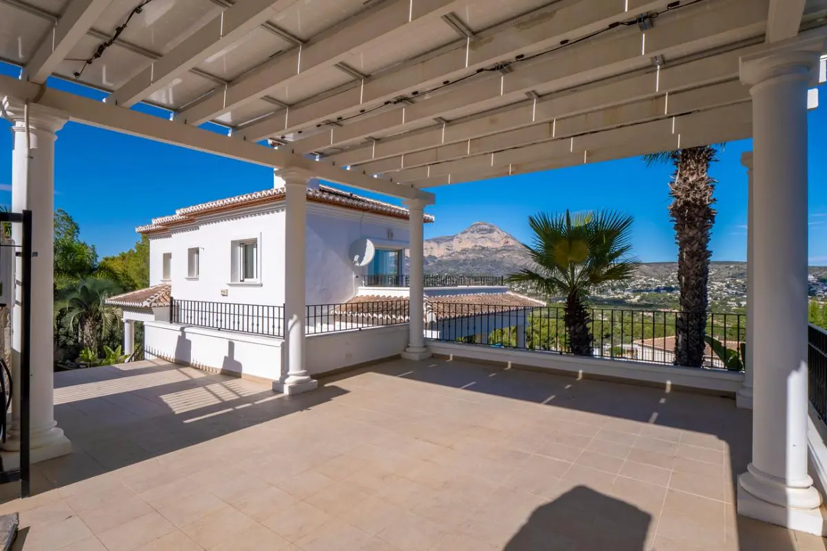 Ruim overdekt terras met witte zuilen en een pergola, met uitzicht op de berg Montgó en het omliggende mediterrane landschap.