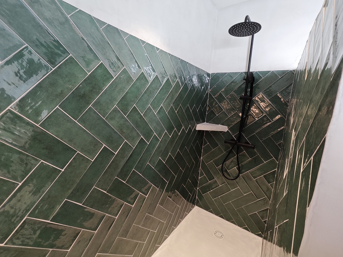 Doucheruimte met glanzende groene tegels in visgraatpatroon, voorzien van zwarte designkranen en een witte douchebak.