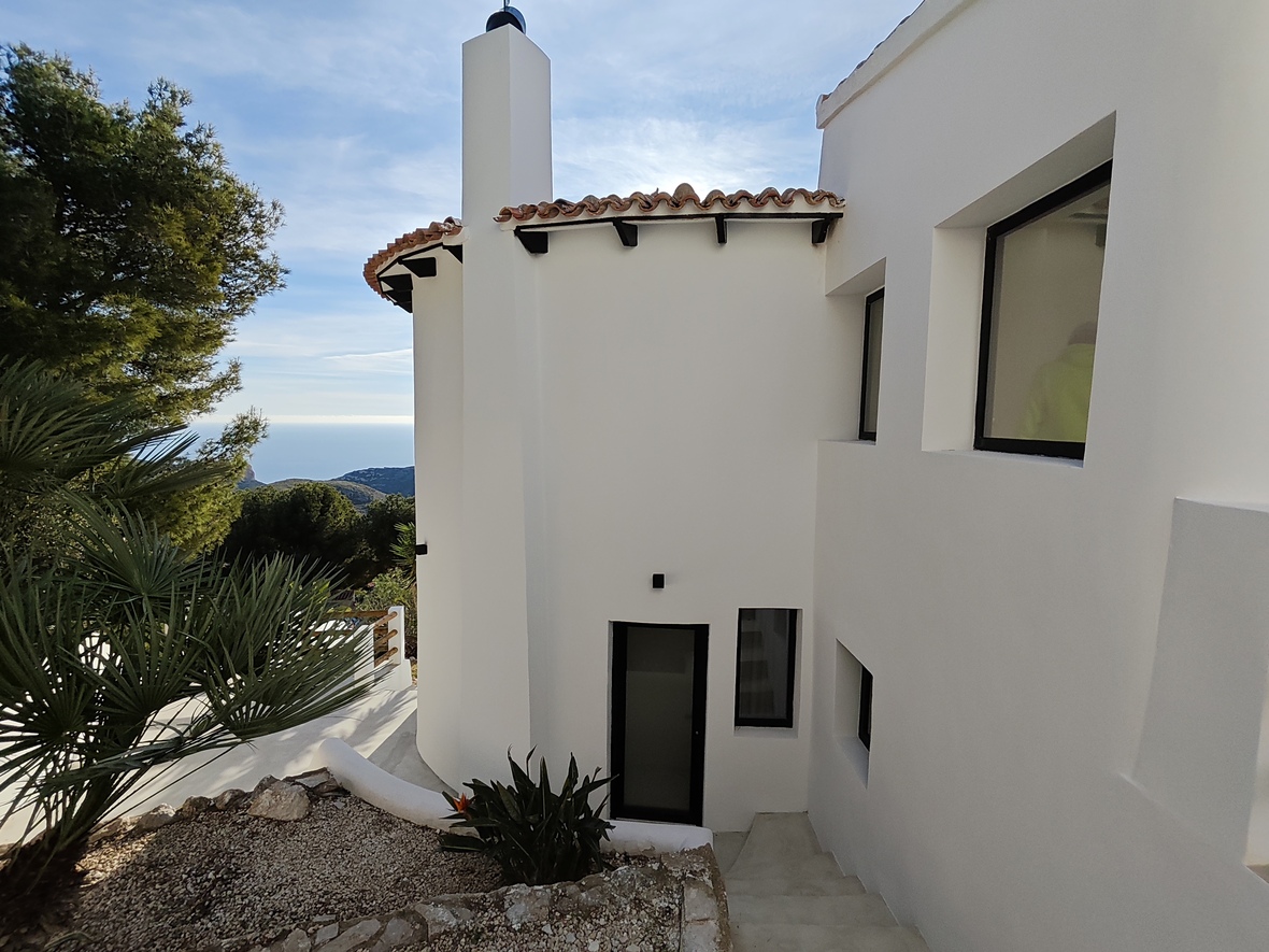 Exterieur van een witte mediterrane villa met een gebogen gevel, terracotta dakpannen en een trap die leidt naar een entree met uitzicht op zee.