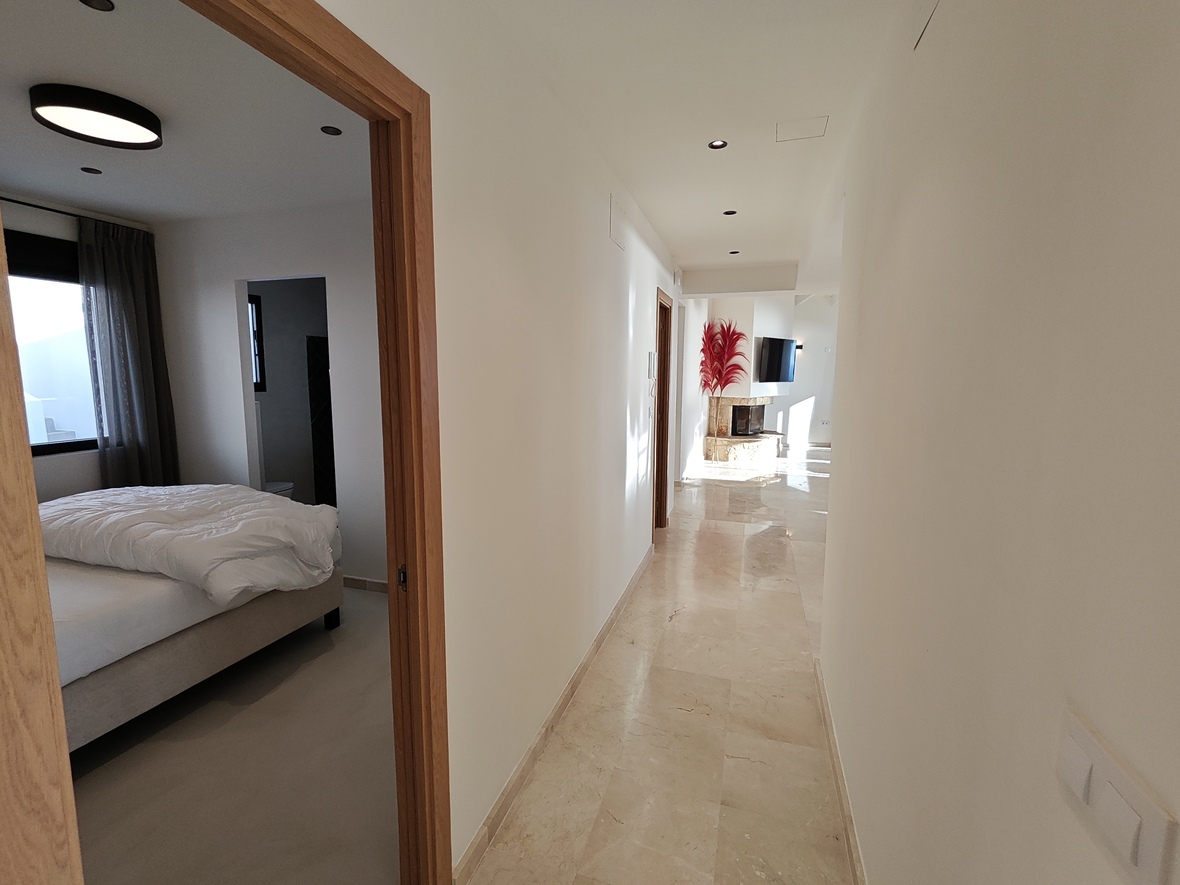 Lichte gang met gepolijste marmeren vloer die leidt naar een woonkamer met stenen open haard en een aangrenzende slaapkamer met houten kozijnen.