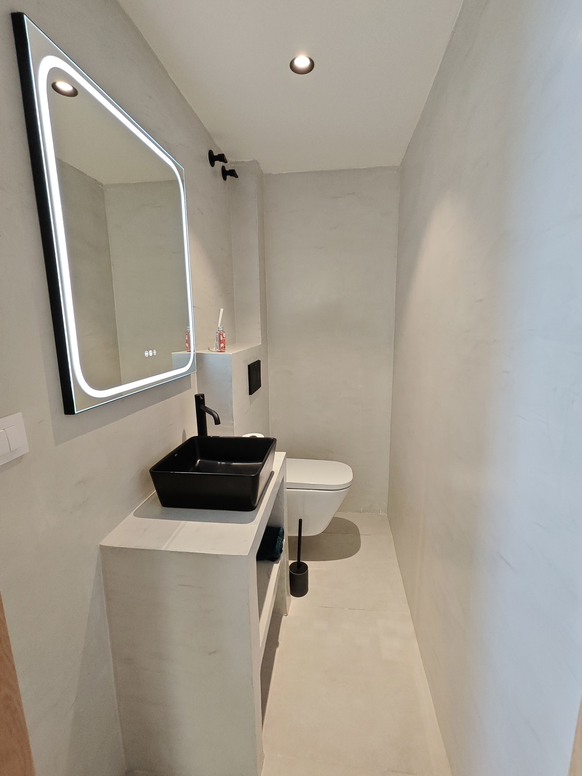 Minimalistische badkamer met een zwarte opzetwastafel, matzwarte kraan, LED-verlichte spiegel en lichtgrijze microcement wanden.