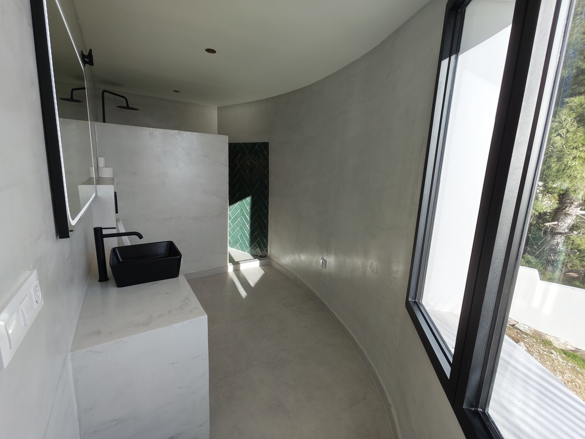 Minimalistische badkamer met gebogen wanden van woonbeton, een zwarte opzetwastafel en inloopdouche met groene visgraattegels.