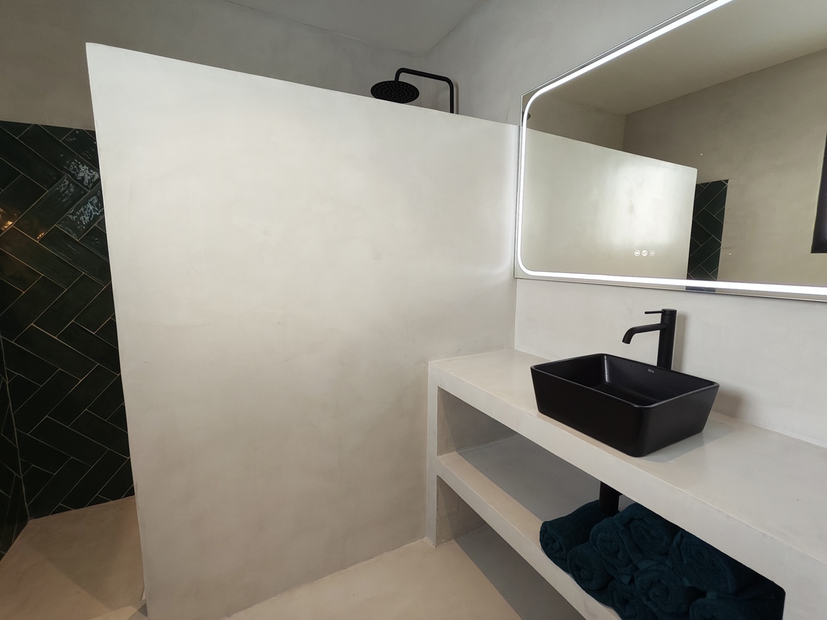 Moderne badkamer met afwerking in microcement, een zwarte opzetwastafel en led-spiegel. De inloopdouche is voorzien van donkergroene visgraattegels en matzwarte kranen.